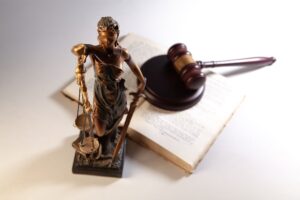Estatueta da deusa da justiça com a balança, ao lado de um martelo de juiz sobre um livro aberto