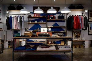 Interior de uma loja de roupas, com araras, prateleiras e mesa de exposição