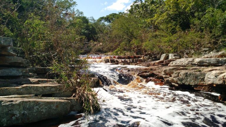 Água do Rio Jacuípe correndo sobre lajes de pedra na Cachoeira de Domingos Lopes, em Morro do Chapéu, com mata verde nas duas margens