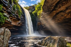 Cachoeira do Agreste em Morro do Chapéu vista do poço, com a queda entre os paredões e raios de sol na névoa