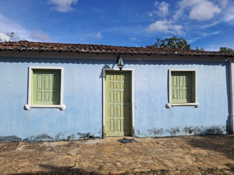 Casa térrea azul-clara da Vila do Ventura com porta e janelas verdes e lanterna sobre a porta