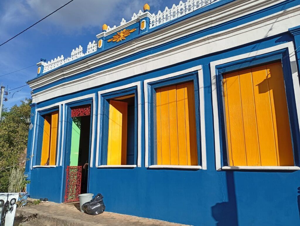 Casa térrea azul da Vila do Ventura com janelas amarelas e platibanda decorada