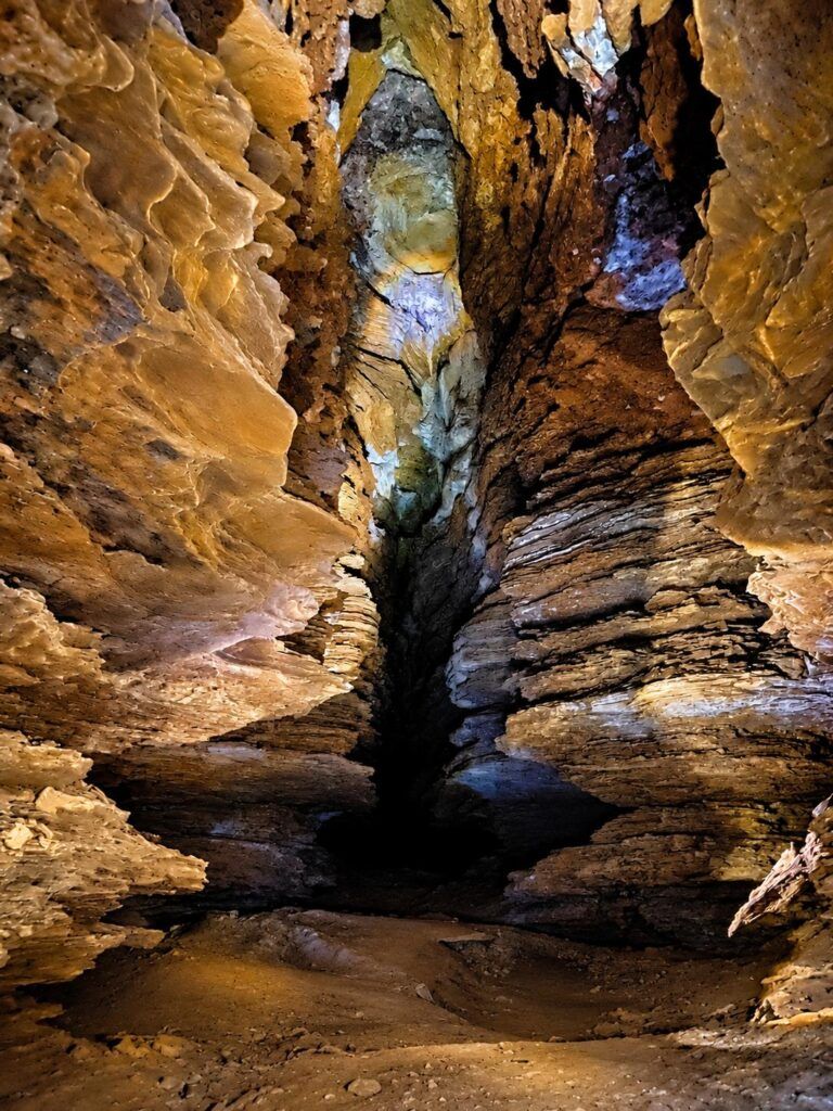 Passagem estreita e alta entre paredes de rocha na Gruta do Cristal, iluminada por lanterna