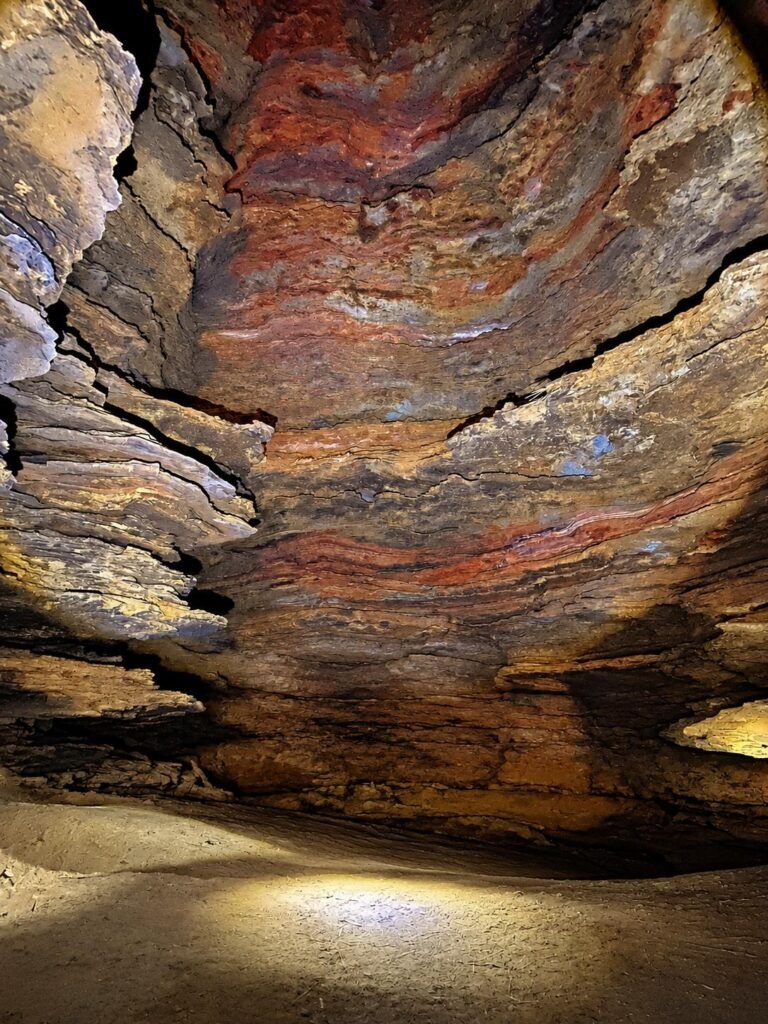 Galeria da Gruta do Cristal com paredes de rocha em camadas finas, em tons de vermelho e cinza