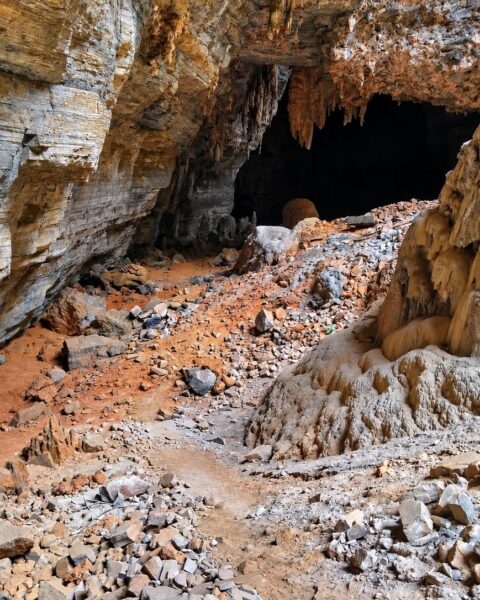 Blocos de rocha e um grande espeleotema diante de uma entrada escura da Gruta dos Brejões, em Morro do Chapéu