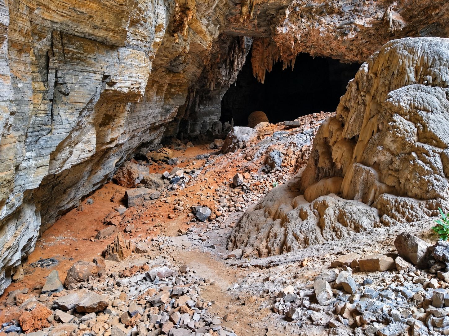 Blocos de rocha e um grande espeleotema diante de uma entrada escura da Gruta dos Brejões, em Morro do Chapéu