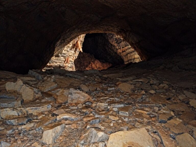 Galeria larga e escura da Gruta dos Brejões, com teto em arco, chão de lajes de pedra e uma passagem iluminada ao fundo