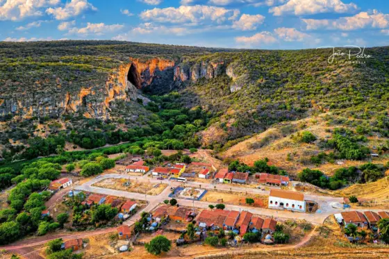 Vista aérea do povoado de Brejões da Gruta, com a entrada da gruta no paredão ao fundo