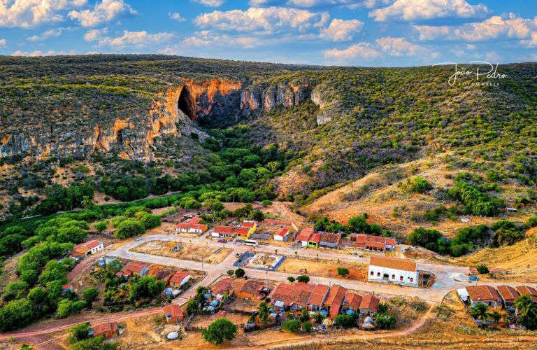 Vista aérea do povoado de Brejões da Gruta, com a entrada da gruta no paredão ao fundo