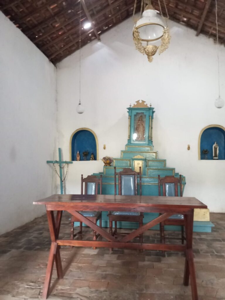Interior da igreja da Vila do Ventura, com o altar azul-turquesa ao fundo e uma mesa de madeira à frente