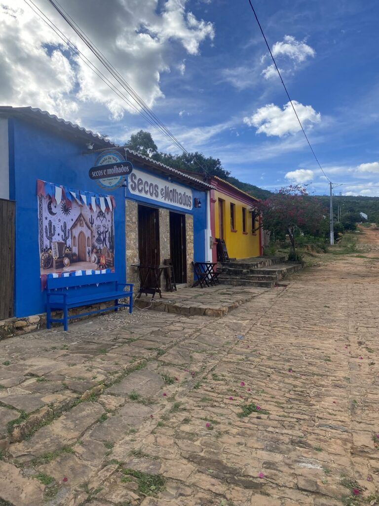 Rua calçada de pedra da Vila do Ventura com uma venda azul e uma casa amarela, e a serra ao fundo
