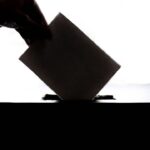 Silhueta de uma mão colocando o voto na urna