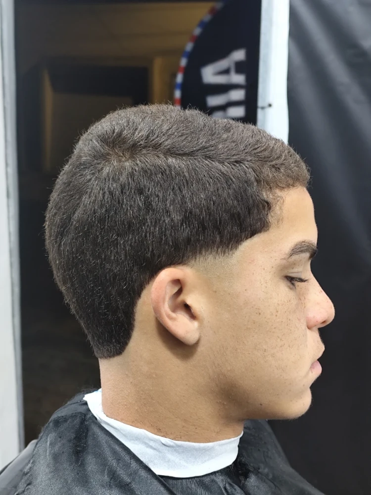Jovem de perfil com corte de cabelo moderno e capa de barbeiro