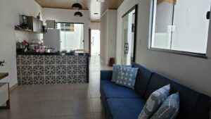 Sala da Casa de Mamãe com sofá azul e a cozinha americana ao fundo