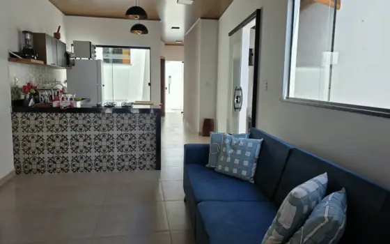 Sala da Casa de Mamãe com sofá azul e a cozinha americana ao fundo
