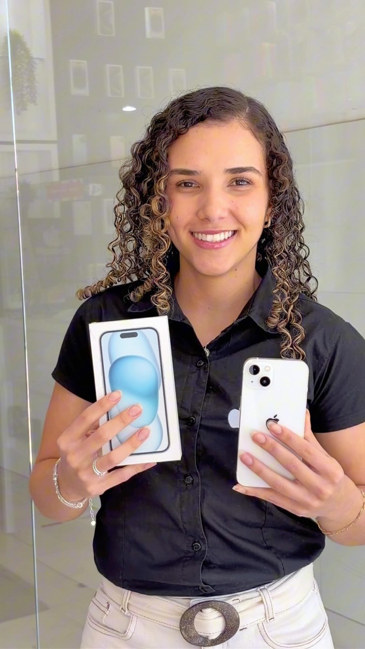 Vendedora sorridente em loja de celulares exibindo iPhone branco e sua caixa