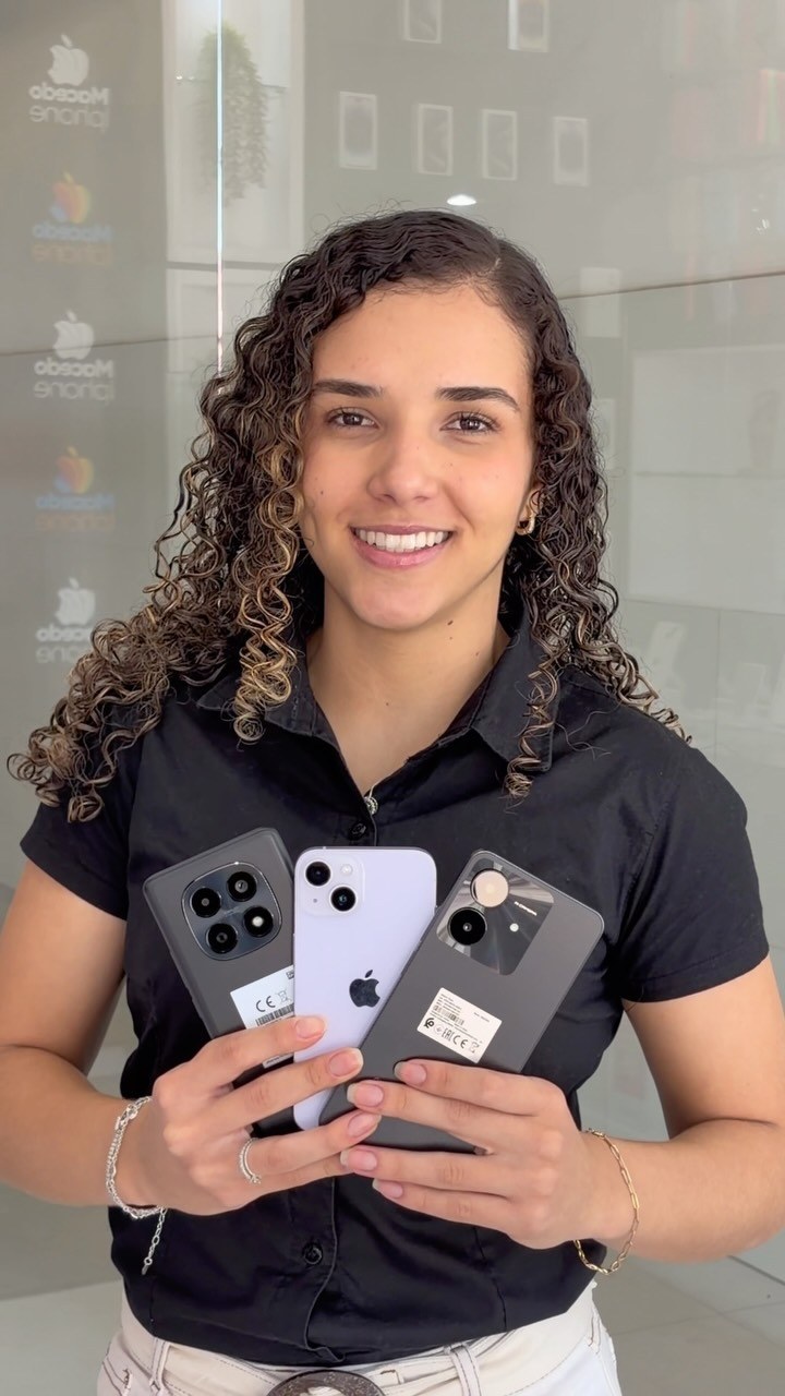 Vendedora sorridente segura três iPhones em loja com vitrine de vidro