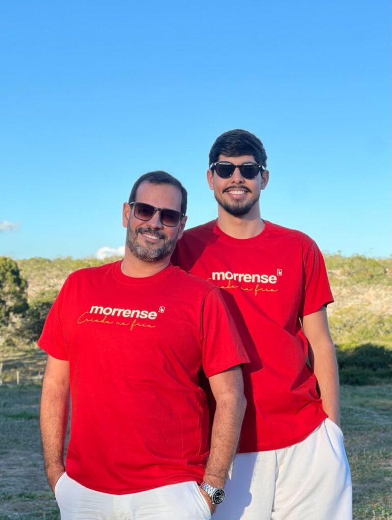 Dois homens de óculos com camisetas vermelhas Morrense da Made in Morro posam ao ar livre
