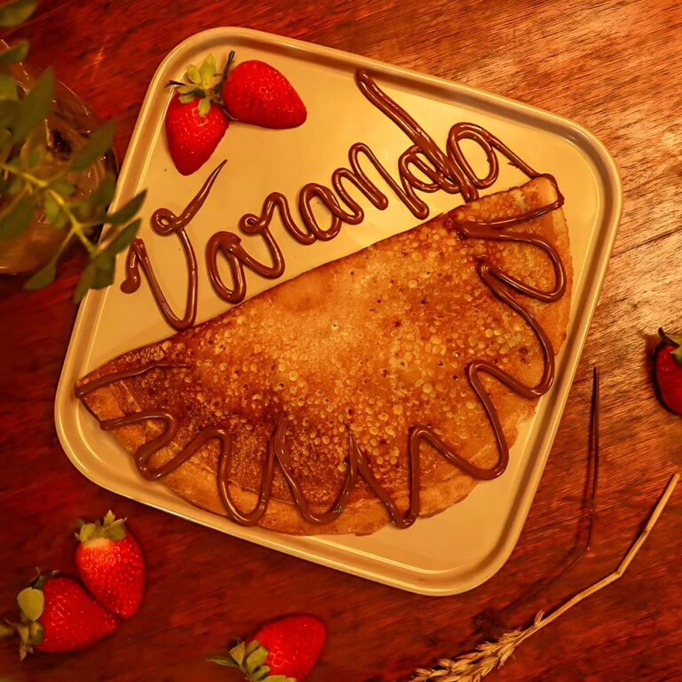 Crepe com calda de chocolate e morangos em um prato sobre mesa de madeira